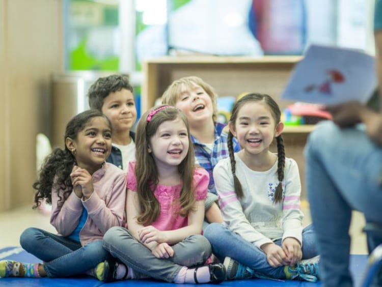 Group of kids laugh sitting on the ground during story time