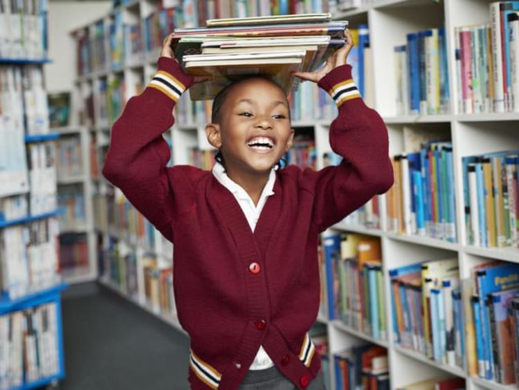 Girl stacks thin books atop her head in library