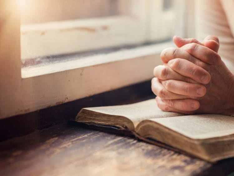 man with folded hands praying on a bible