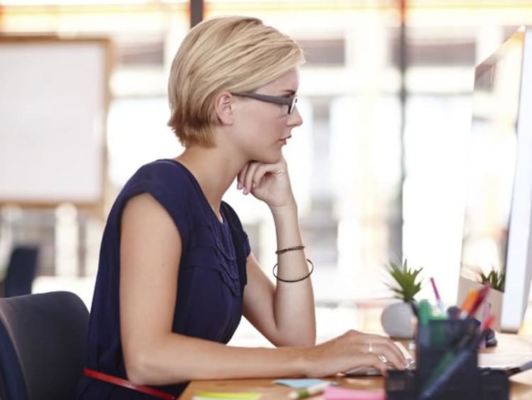 Professional woman with short hair uses a Mac desktop in office space