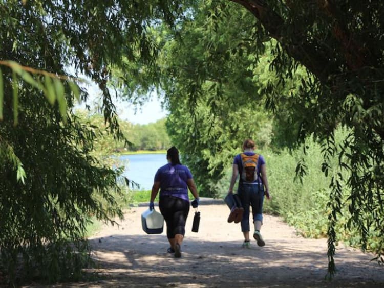 Two people walk up to a lake with equipment in their hands