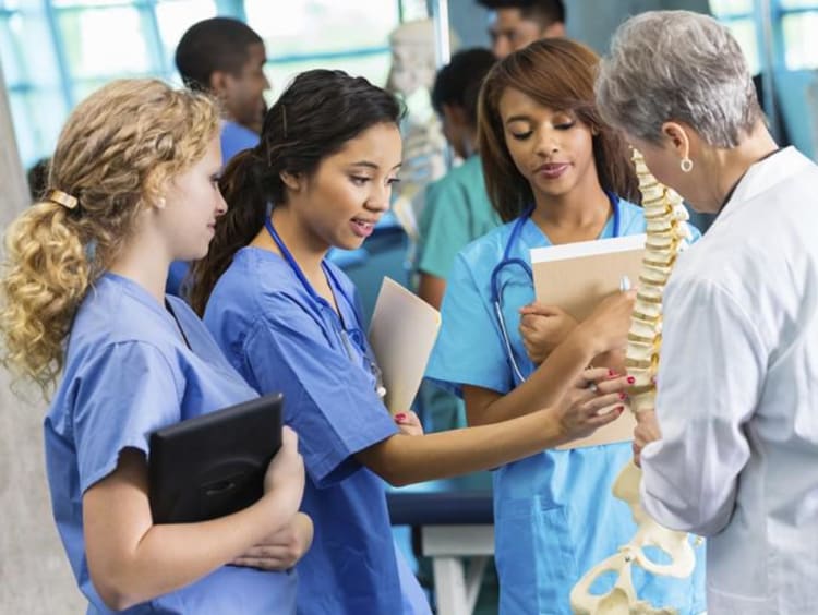 three nursing students and professor looking at a skeleton