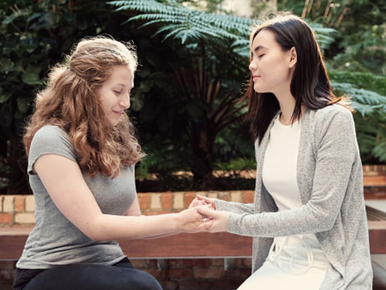 Two girl friends praying on a bench together showing humility before God