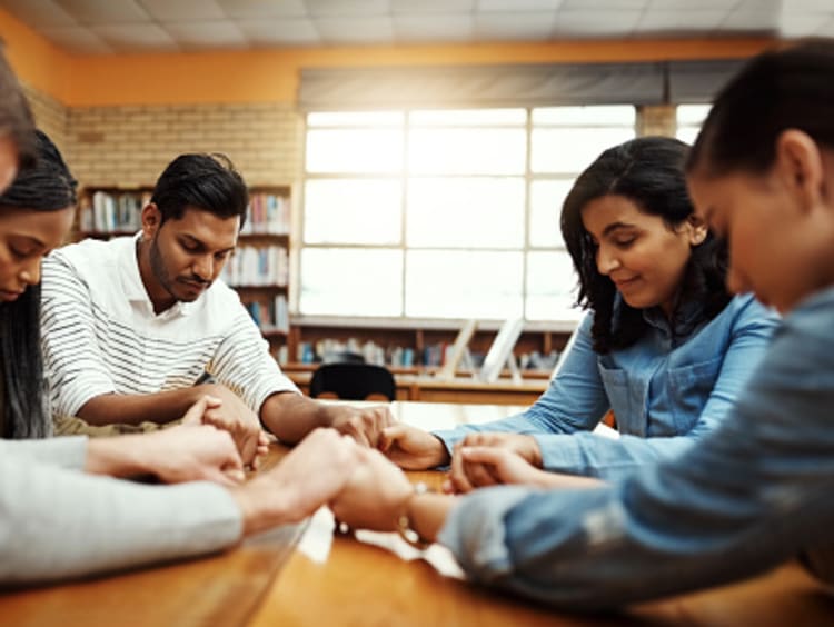 interracial group of people gathered around a workplace library table praying as an integration of faith