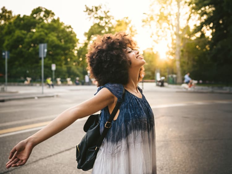 Curly-haired woman has arms open enjoying the sunlight in an empty parking lot