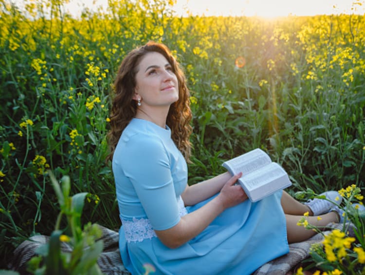 Woman looking up after reading her Bible in a field of flowers for spiritual cleansing