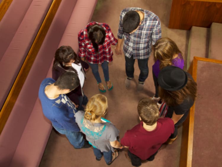 Christians standing and holding hands while praying for one another near church pews