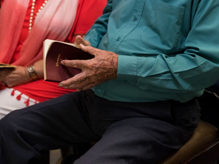 Older couple sitting next to each other open hymnals in a Christian community church