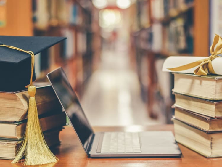 A stack of books next to a graduation cap and a laptop