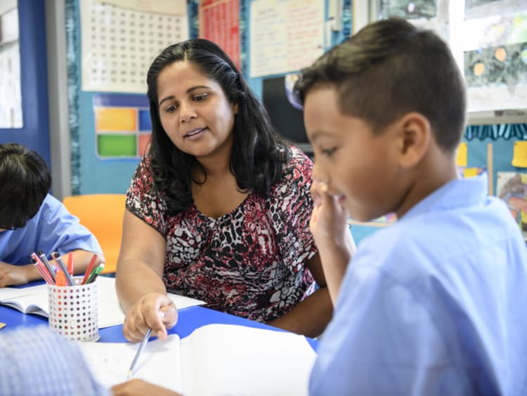 A female multicultural teacher helping a student with his assignment