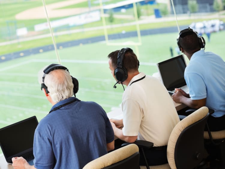 Three news broadcasters sitting side by side in sports stadium