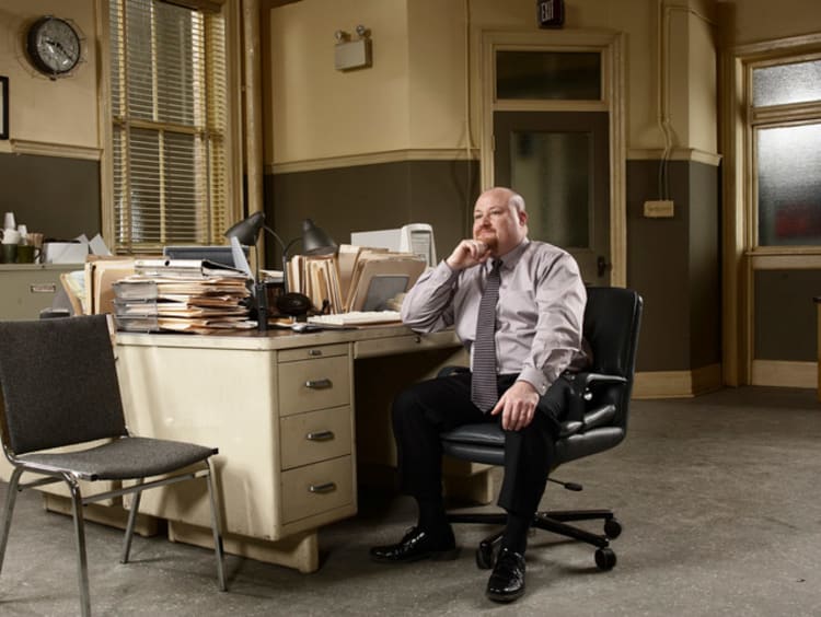 Private investigator sitting at desk covered in paperwork