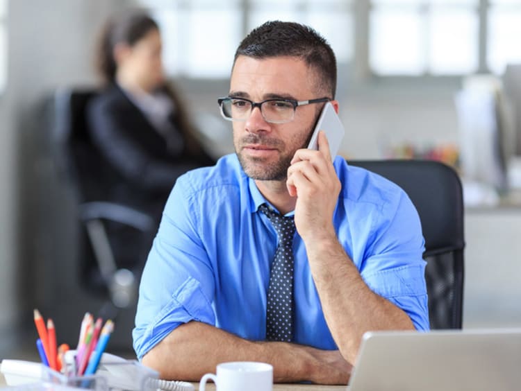 man with glasses speaking on phone in office