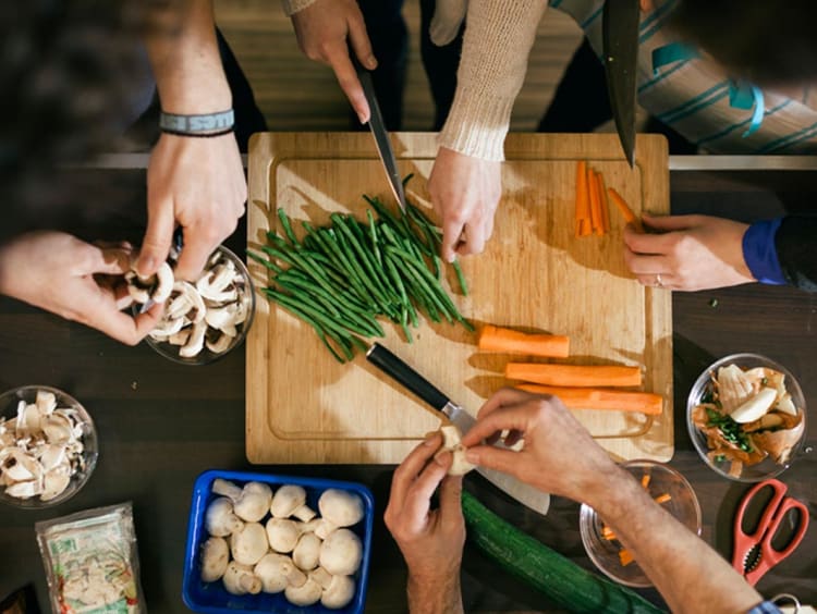 diverse hands prepare food around a cutting board in kitchen setting