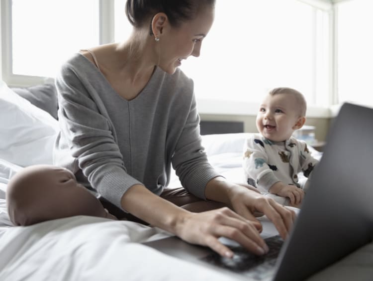 Woman working in bed on a laptop with her child