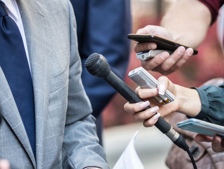 broadcast journalists hold microphones in front of a business man conducting a press conference interview