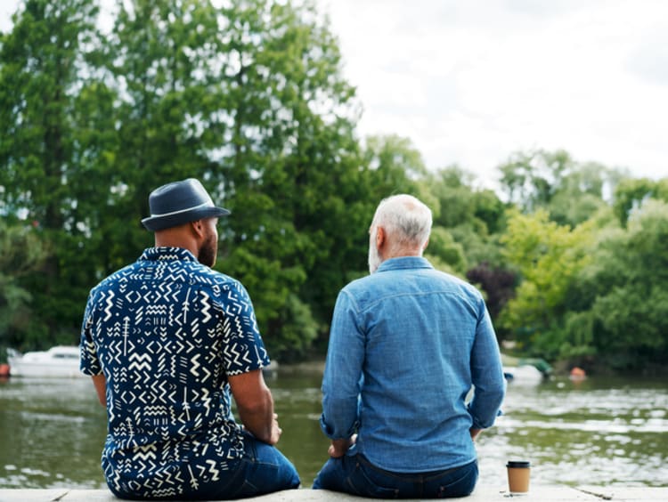 Two men talking, sat next to river