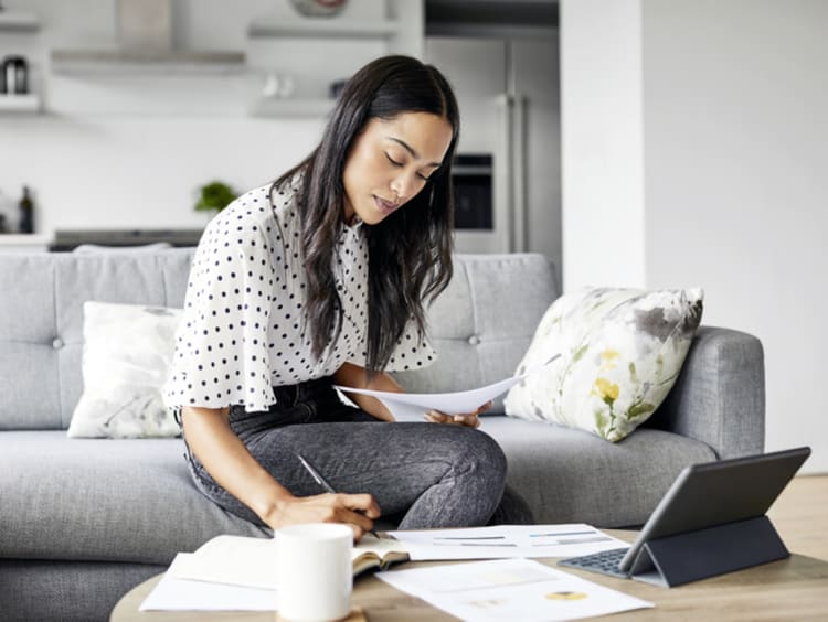 Woman sitting on gray couch in professional wear working on finances at home