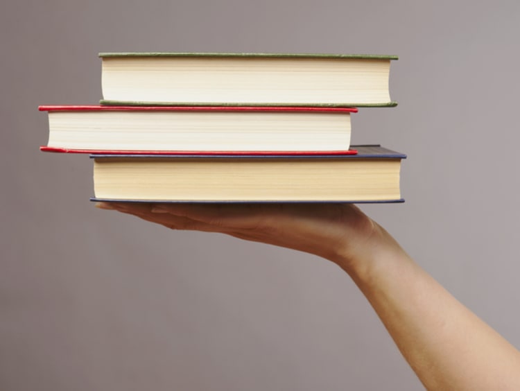 A hand holding up three books