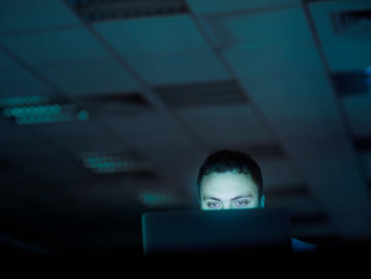 Male cybersecurity professional works on his computer at night