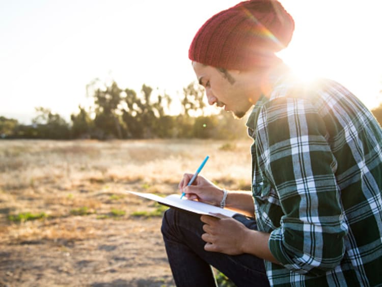 A male college student practicing daily journaling by writing outside alone