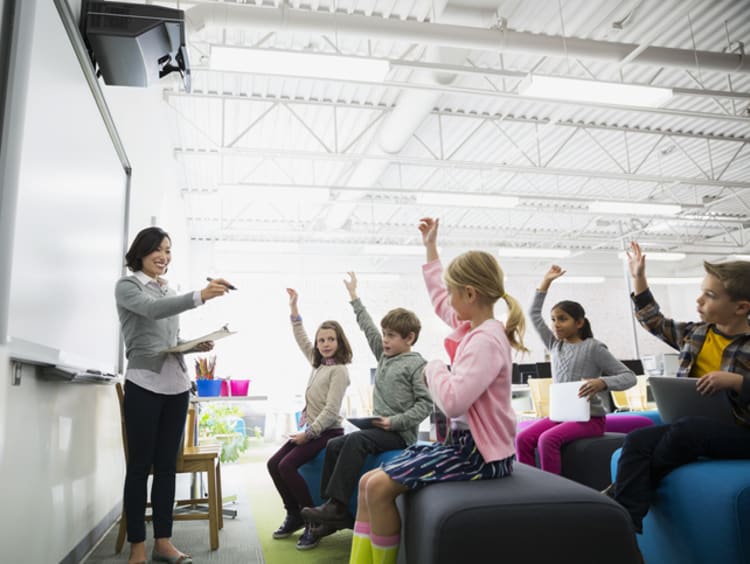 A classroom full of elementary students raising their hands