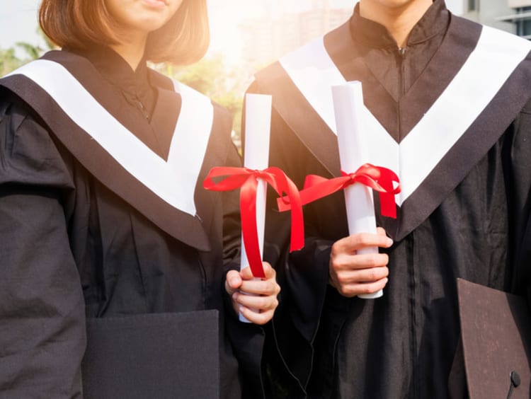 Two college graduates holding their diplomas and wearing their cap and gown