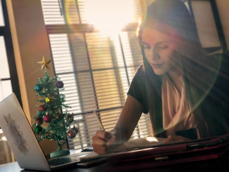 A girl working on homework by a Christmas tree