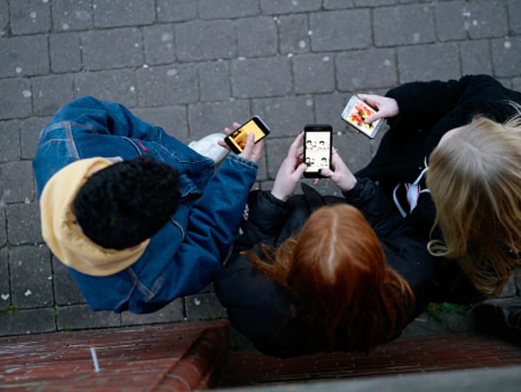 Three friends looking at examples of new media on phones