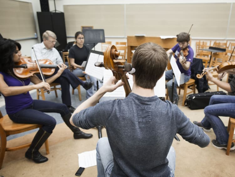 Orchestra students playing string instruments in a classroom