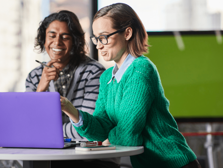 Two students work at laptop in office setting