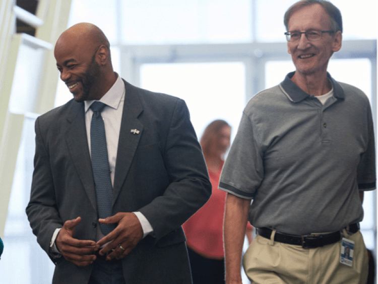 Education leaders and faculty walk and chat down a school hallway