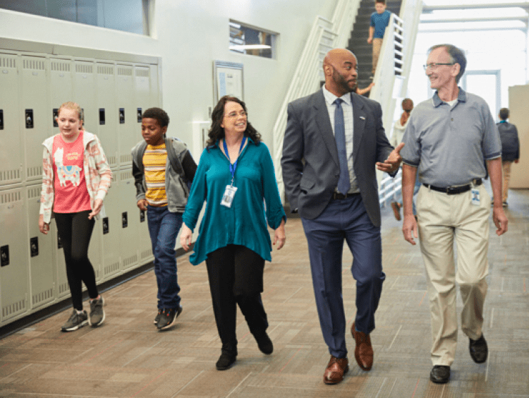 faculty, educational leaders and students walk and talk in a school hallway