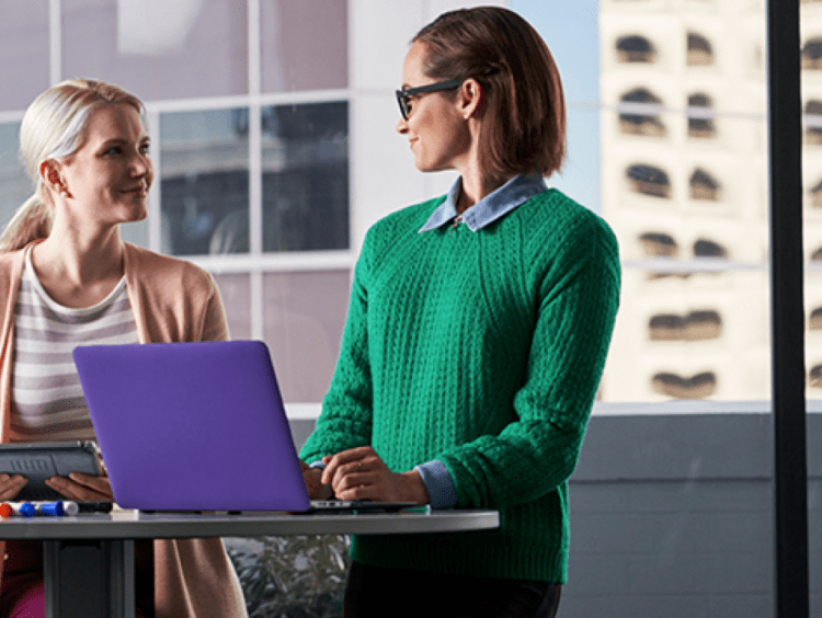 Two women students work at laptop in office setting