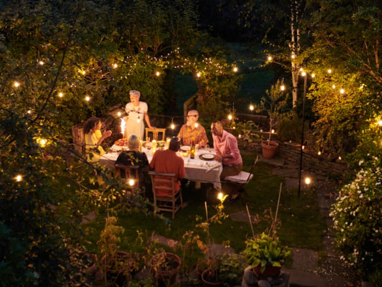 Friends having dinner together outdoors with clear lights in the trees