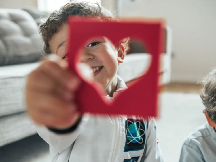 Little boy holding up heart cut out of paper