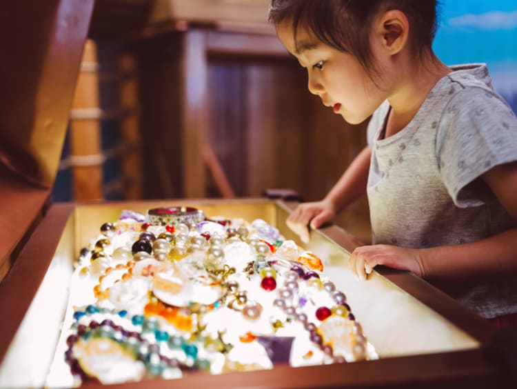 Little girl looking at pearls and other jewelry treasure in a chest