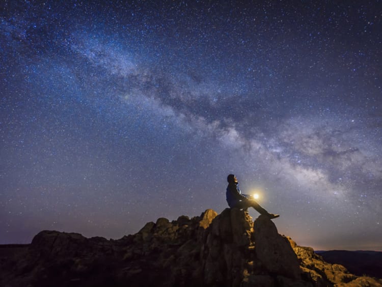 Man sitting on rocks looking up at the stars with beautiful starlit sky above him