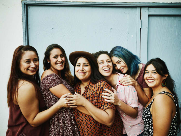 Group of multicultural women do a group photo together in front of a blue wall