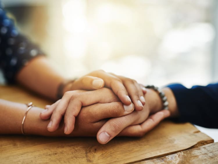 Woman clasps both hands around another's hand on a table