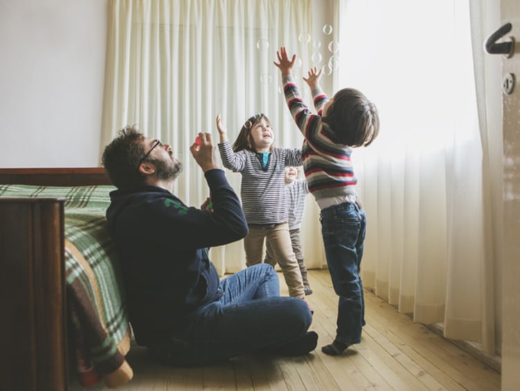 Two young boys play enthusiastically with dad blowing bubbles in bedroom