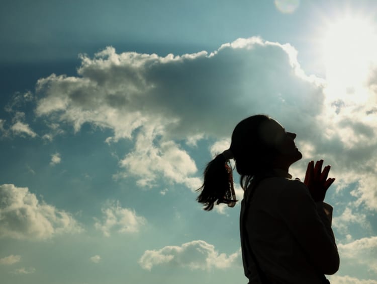 Woman smiles looking up to the sun with clouds in the sky behind her