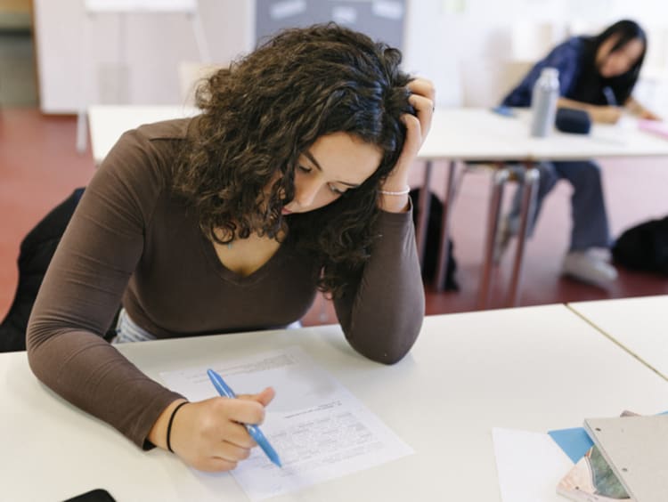 Female student working at desk in classroom feeling pain and suffering