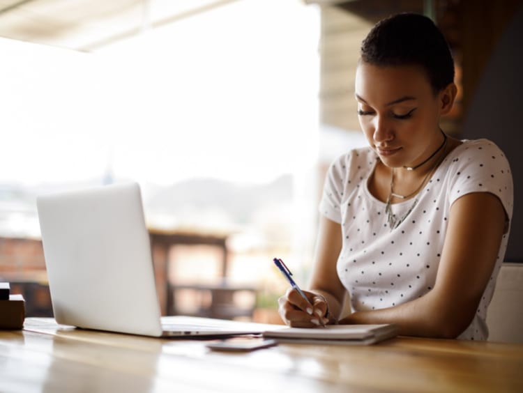 a student taking notes for a class while working on her laptop