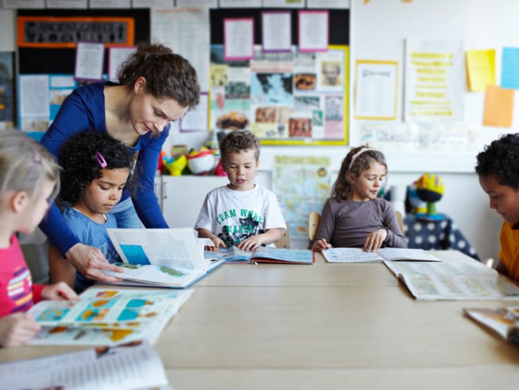 A group of elementary students reading books together with their teacher