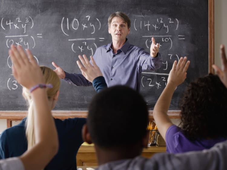 male teacher in front of chalkboard teaching students