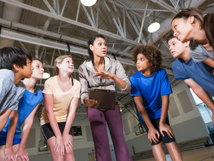 A PE teacher in a huddle with a group of her students