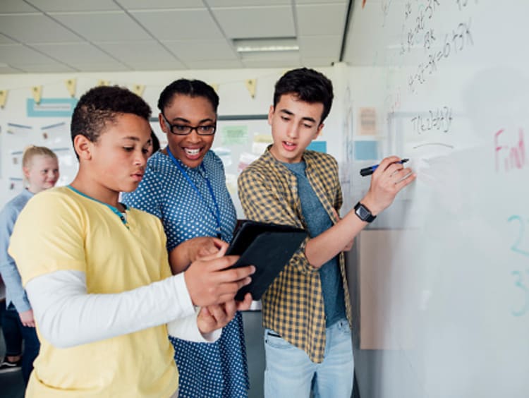 Three students solving a problem at a whiteboard during a multi-discipline lesson