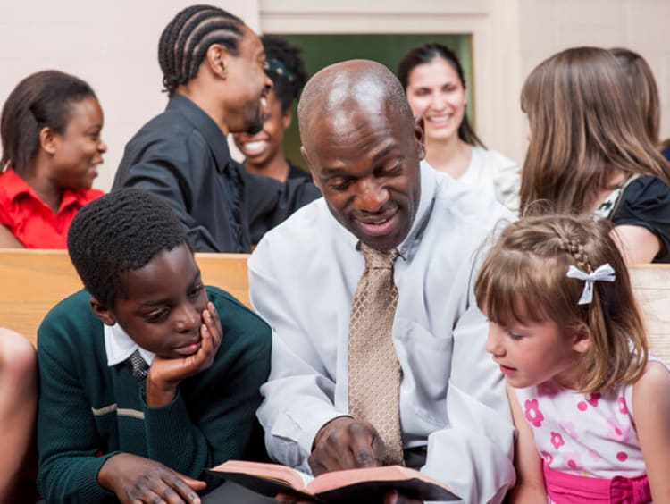 Diversity in the church with African-American man pointing in Bible to children