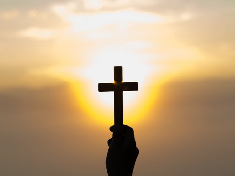 Man holding cross in hand against sunset sky